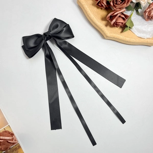 Detail of elegant black satin bow hair clip with long ribbons on a vintage background