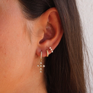 Detailed view of layered golden cross earrings set with zircon stones on a model ear