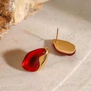 Macro shot of irregular red resin earrings with gold metal base on stone background