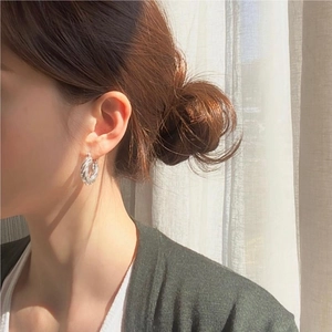 Detail view of silver twisted rope hoop earrings worn by a model in soft sunlight