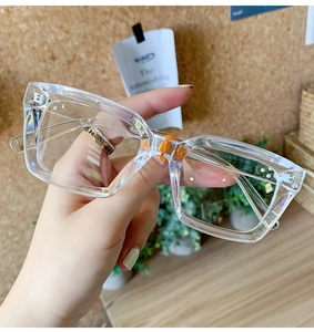 Detail of transparent square oversized glasses frames held by hand in a warm home setting