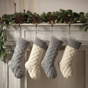 Detail of four knitted Christmas stockings in grey and beige hanging on a fireplace mantel