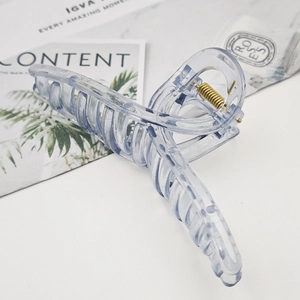 Detail of transparent light blue hair claw clip with golden metal spring on marble surface