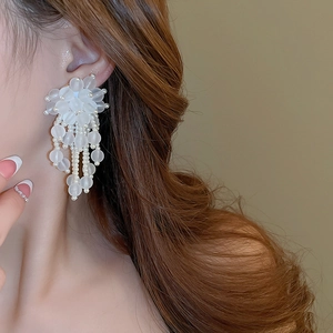 Close-up of white acrylic flower tassel earrings with pearls on model side profile