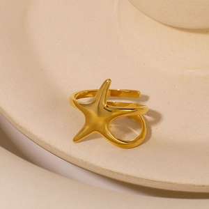 Modern minimalist gold star wrap ring displayed on a warm beige ceramic bowl edge