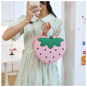 Close-up of pink strawberry shaped shoulder bag with green sequins on a model