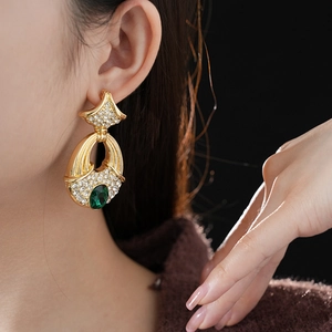 Close-up of vintage gold ginkgo leaf earrings with green gemstone and pavé diamonds