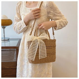 Detail of straw crossbody bag with white lace bow and shoulder strap in brown color