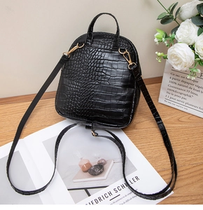 Detail of black crocodile texture mini backpack with adjustable straps on wooden desk