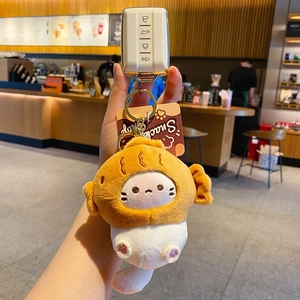 Cute white cat plush keychain wearing fish costume held in a cafe setting