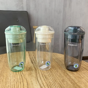 Trois shakers de sport Casno vert, transparent et gris sur une table en bois