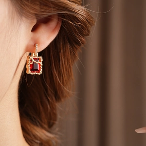 Détail boucles d'oreilles carrées dorées avec grande pierre rouge et zircons brillants