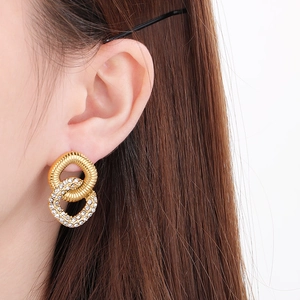Macro detail of gold-plated double-loop earrings with crystal pavé and twisted metal texture