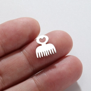 Macro shot of silver metal comb charm with heart cutout handle held between fingers