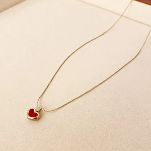 Gros plan détaillé du collier doré avec pendentif cœur rouge et pompon en gourde