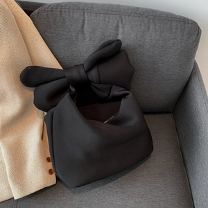 Chic black quilted puffer hand bag with oversized bow design on a stylish sofa