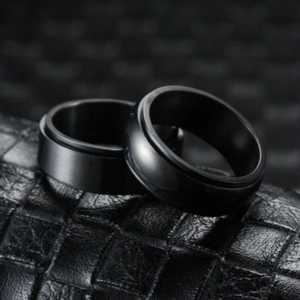 Close-up of black rotatable anxiety rings on a premium black crocodile leather texture