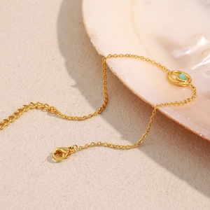 Detail of a gold-plated stainless steel bracelet with a round green gemstone on a shell