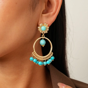 Close-up of Bohemian gold hollow earrings with turquoise beads and rhinestones on a model