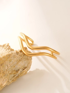 Detailed view of polished golden double-layered wavy cuff bracelet on a stone texture