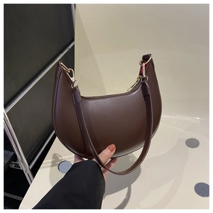 Detail view of dark brown crescent bag with smooth leather texture and gold hardware
