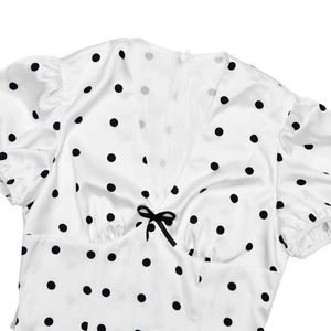 Close-up of white satin dress with black polka dots, V-neck, and bow detail