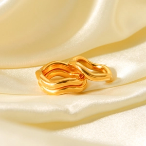 Detailed macro view of three wavy gold-plated stainless steel rings on satin fabric
