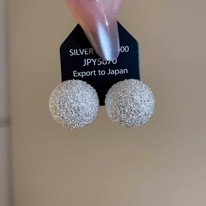 Detail showing round textured silver stud earrings on a black display card with silver hallmark