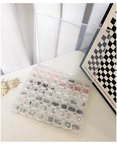 Macro view of transparent acrylic 56-compartment jewelry organizer box on white fabric