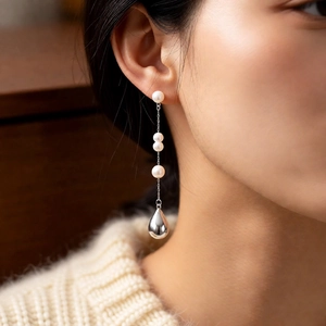 Close-up of a model wearing French vintage pearl drop earrings with silver chain details