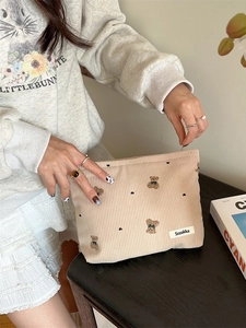 Beige corduroy makeup bag with cute bear embroidery held by a model in a warm setting