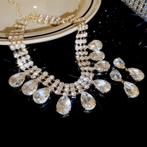 Close-up of gold water drop fringe necklace and earring set with crystals on black surface