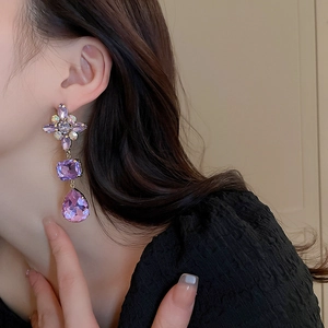 Detail of elegant purple crystal flower drop earrings worn by a model in natural light