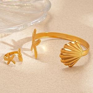 Detail of gold starfish and shell open bracelet and ring set on stone texture