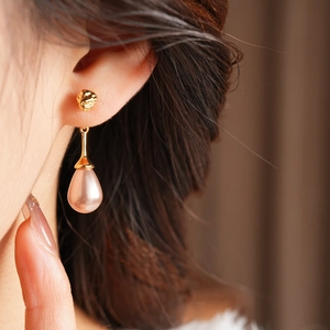 Detailed view of elegant gold drop earrings with pink teardrop pearls on a model