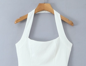 Detail eines weißen Neckholder-Kleids aus strukturiertem Faltenstoff am Kleiderbügel