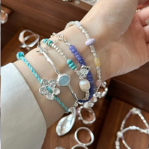 Close-up of stacked blue floral bracelets and silver gemstone bangles on a woman's wrist