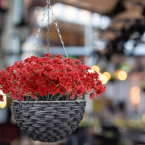 Close-up of artificial red violet flowers in a dark gray woven hanging basket with metal chain