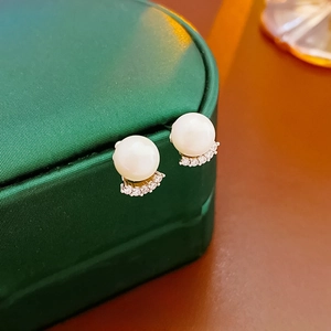 Close-up of gold-plated pearl earrings with zircon inlay on luxury green silk display