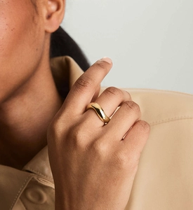 Macro detail of high-polish gold wavy ring on hand showing modern wave design