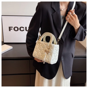 Quilted off-white crossbody bag with pearl embellishments and bow chain detail on model