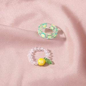 Detail of acrylic lemon ring and crystal beaded fruit ring on soft pink silk