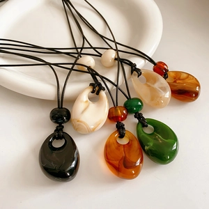 Detailed view of colorful teardrop resin pendants with hand-woven wax ropes in a ceramic tray