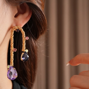 Detail of vintage gold woven earrings with purple and blue teardrop stones on ear