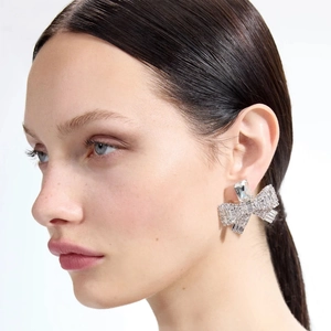 Detailed view of silver bow-shaped rhinestone drop earrings worn by a fashion model