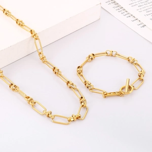 Detailed shot of golden paperclip chain necklace and T-bar bracelet set on white marble