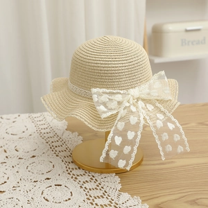 Vue détaillée du chapeau de paille avec nœud en dentelle blanche et cœurs brodés