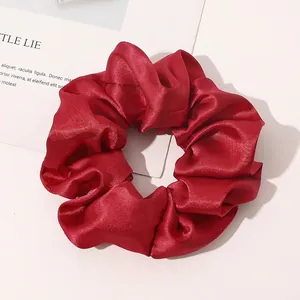 Detailed view of vibrant red silk satin scrunchie with elegant pleated fabric texture