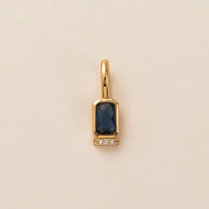 Detail of a gold pendant with a square dark blue gemstone and three round clear stones