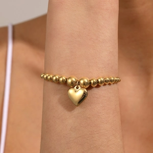 Close-up of a gold ball chain bracelet with a heart pendant worn on a female wrist